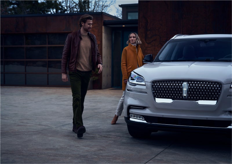 A man and a woman approaching a 2023 Lincoln Aviator® SUV, which illuminates certain lights when they are close | Vance Lincoln in Miami OK
