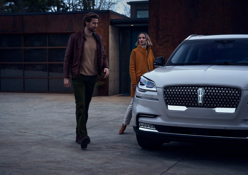 A man and a woman approaching a 2024 Lincoln Aviator® SUV, which illuminates certain lights when they are close | Vance Lincoln in Miami OK