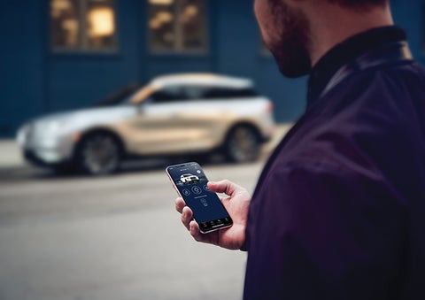 A person is shown interacting with a smartphone to connect to a Lincoln vehicle across the street. | Vance Lincoln in Miami OK
