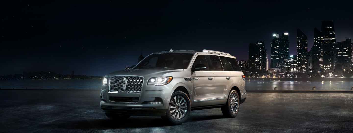 A 2024 Lincoln Navigator® SUV is parked near a city's riverside walk at night