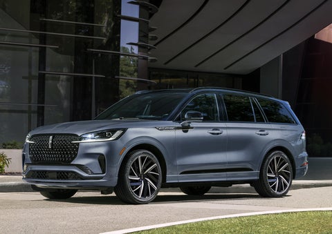 A gray 2025 Lincoln Aviator® SUV is parked outside a modern building showcasing the driver’s side of the vehicle. | Vance Lincoln in Miami OK