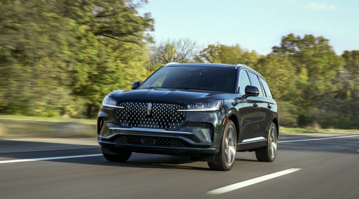 A 2026 Lincoln Black Label™ Aviator® SUV is being driven down a road lined with trees. | Vance Lincoln in Miami OK