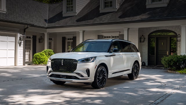 A white 2026 Lincoln Aviator® SUV is parked in the driveway of a luxury home. | Vance Lincoln in Miami OK