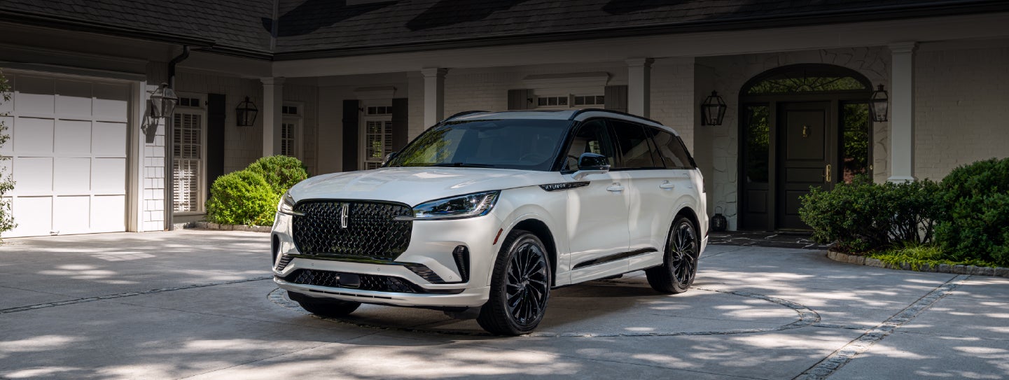 A white 2026 Lincoln Aviator® SUV is parked in the driveway of a luxury home. | Vance Lincoln in Miami OK