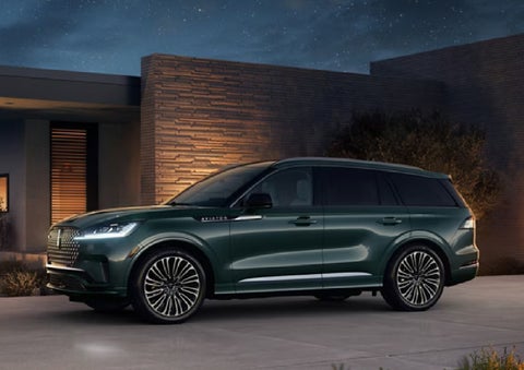 A green 2027 Lincoln Aviator® SUV is parked outside a contemporary home. | Vance Lincoln in Miami OK