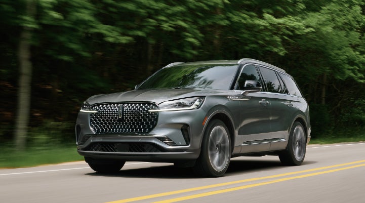A 2027 Lincoln Aviator® SUV is being driven down a road lined with trees. | Vance Lincoln in Miami OK